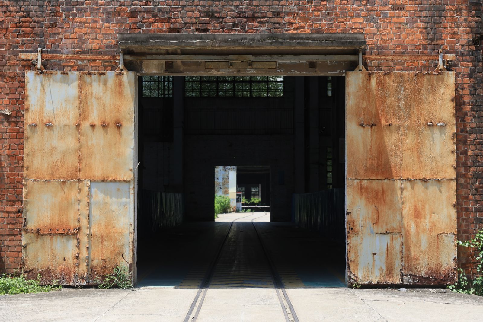 A rustic brick factory entrance with open, weathered metal doors bathed in sunlight.